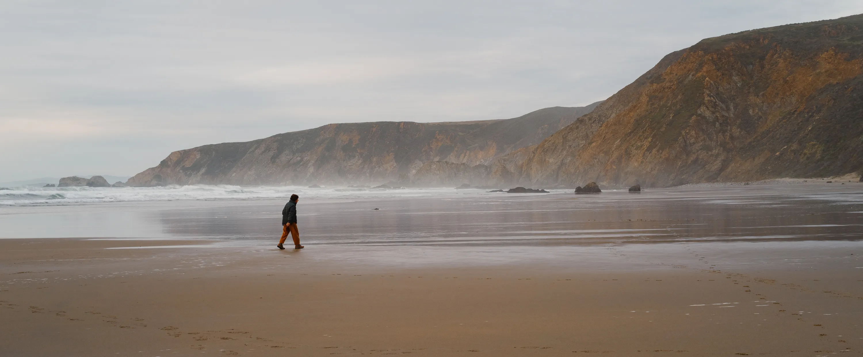 A lone person walks along a long, empty beach