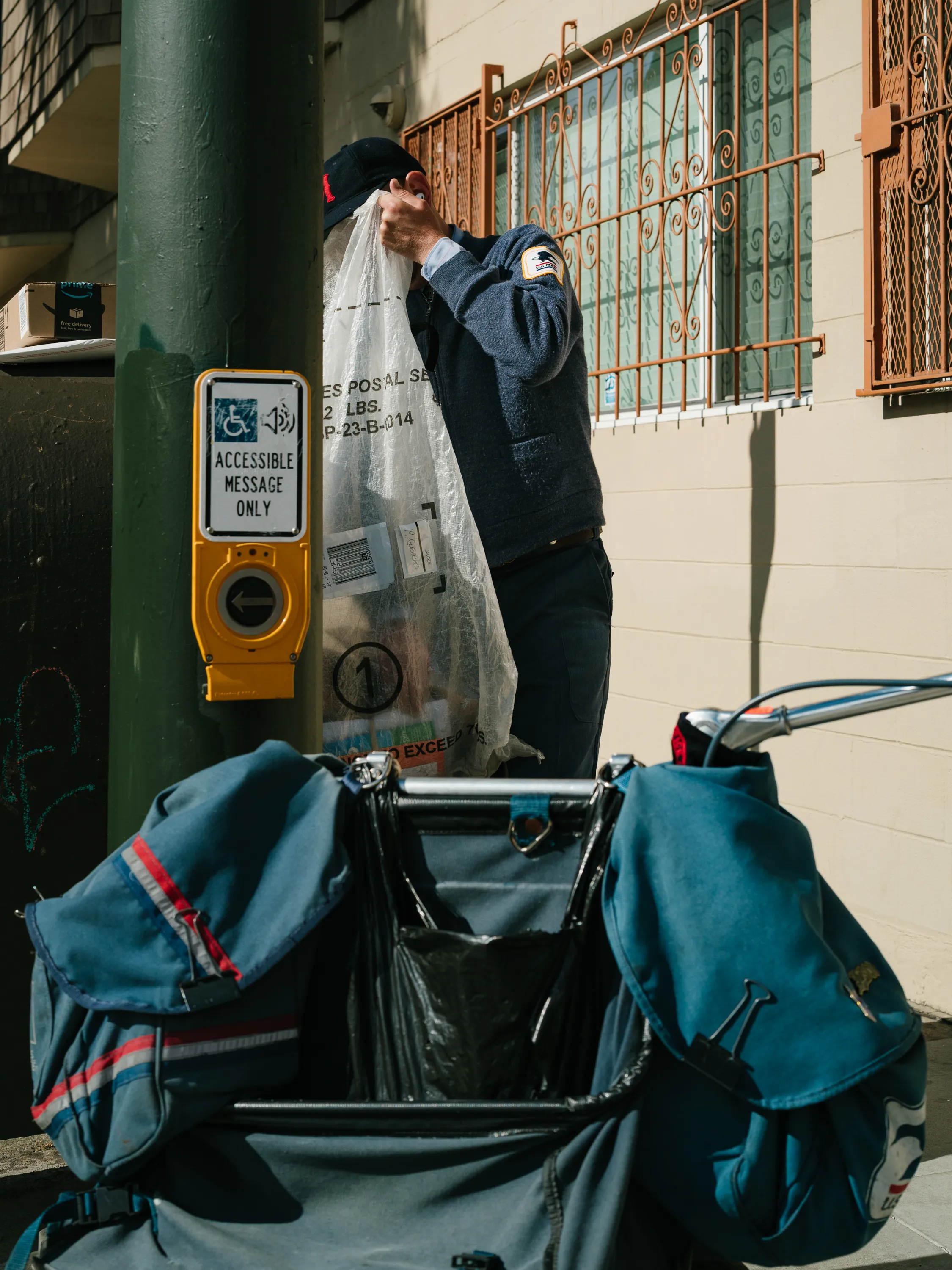 A postman collects letters and packages from a sidewalk mail drop