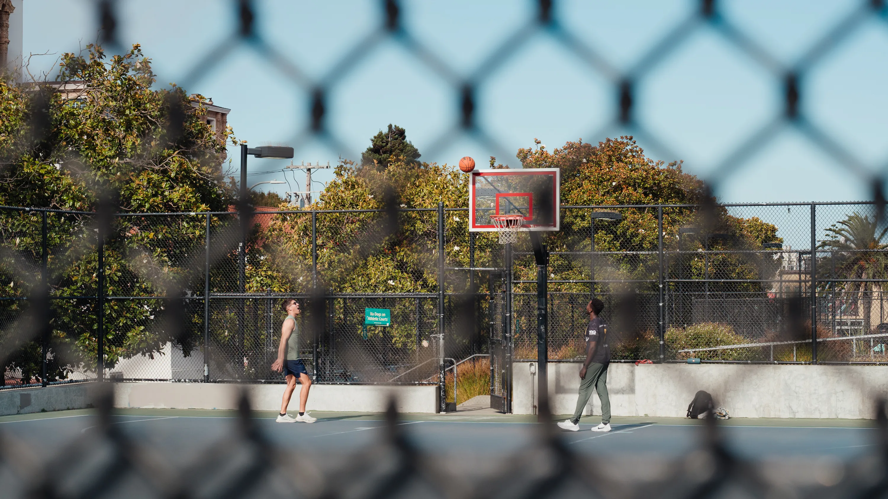 Two men watch to see whether a basketball will go in the hoop