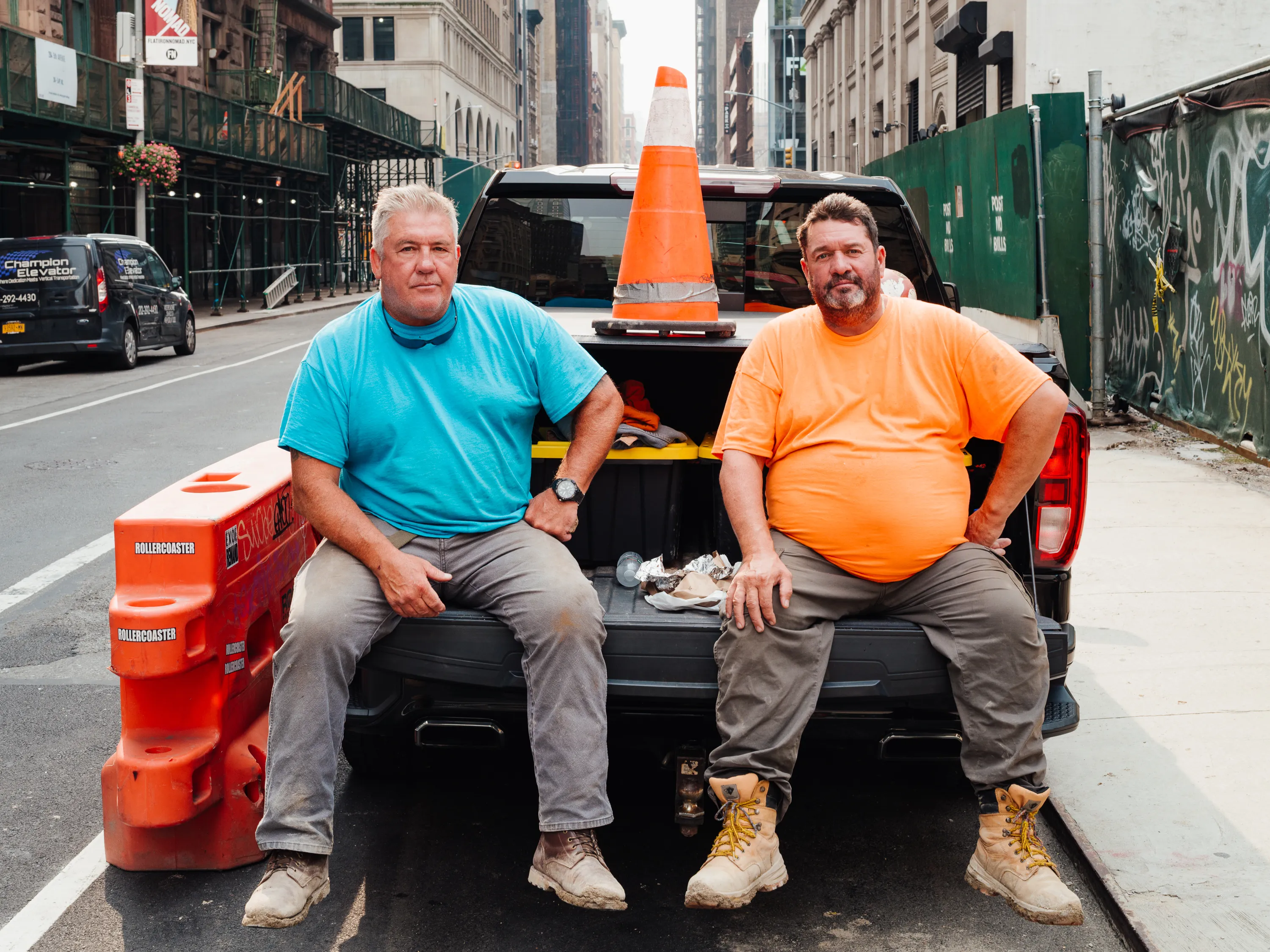 Two men sitting in the back of a pickup truck pose for the camera