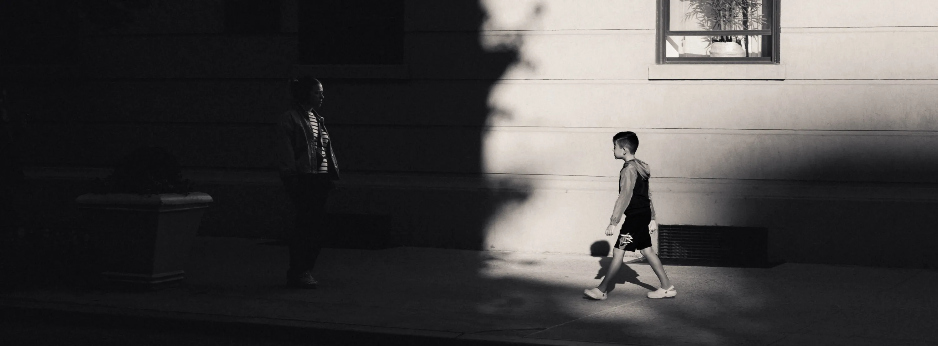 A mother looks on from the shade as her son walks closer out of the light